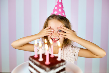 Little blonde girl in pink birthday cap smiling, close her eyes, make a wish