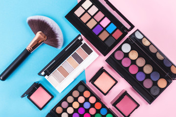 Wall Mural - Makeup and beauty products on pink and blue background. Eye shadow palettes. fan contouring brush and blushes. Flatlay, top view. 