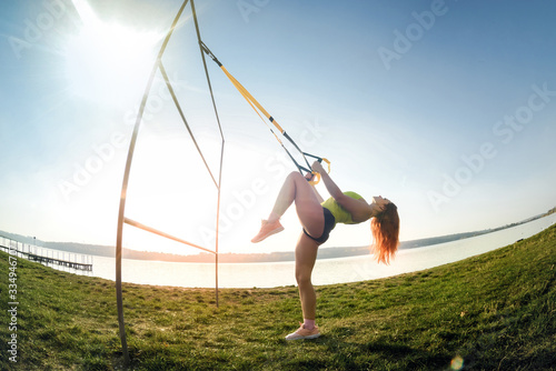 Cuadros en Lienzo beautiful woman exercising with suspension straps TRX outdoors near the lake at daytime