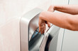 A woman in a public place dries his hands in an electric dryer