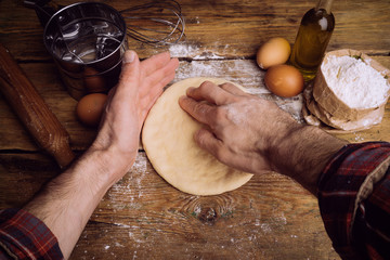 Pizza dough cooking in the home kitchen. Homemade dough for bread, pizza, pastries and rolls. Dough ingredients (flour, eggs, butter) on a wooden rustic background