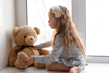 child little girl sitting on a windowsill with a teddy bear