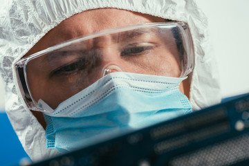 engineer in protective goggles and medical mask holding computer component