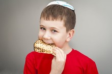 Cute Caucasian Child In A White Kippah Cap Eating Shmura Matzo, A Piece Of Traditional Jewish Unleavened Bread For Pessakh, Jewish Passover Holiday.