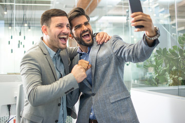 Wall Mural - Two men in business wear taking a crazy selfie in office