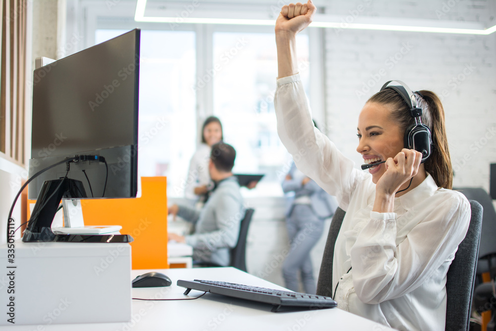 Euphoric female call center worker with headset celebrating a good job in the workplace