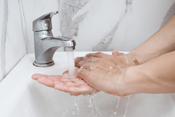 Wall Mural - Young man washing hands over sink in bathroom, closeup, Corona virus or Covid-19 prevention, hygiene to stop.