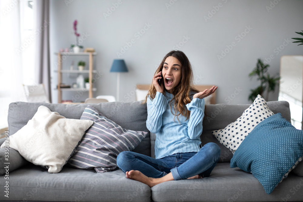Woman emotionally talking on a mobile while sitting at home on the couch. Portrait of a positive girl. - obrazy, fototapety, plakaty 
