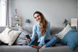 © BestForYou - Online chat. Smiling woman talking on smartphone with friends while sitting on sofa at home.