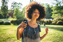Young Black Woman Dancing Listening To The Music With Earphones From The Smart Phone In A Park At Sunset On A Summer Day
