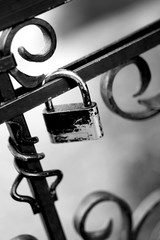 Close up of a shriveled padlock locked on an iron fence black and white photography