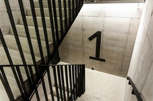 Huge First Floor Sign In The Staircase. Concrete Walls And Steel Handrail