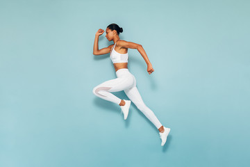 sports woman running in studio. full length shot of young female exercising over blue backgroud.
