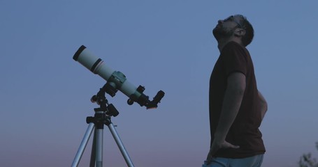 Wall Mural - astronomer with a telescope watching at the stars and moon with blurred city lights in the backgroun