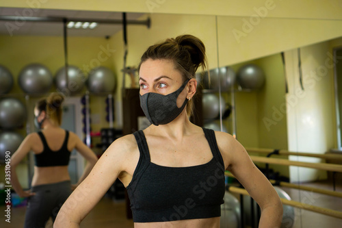 Young female athlete woman put on black designer protective mask sitting in empty gym. We are strong to stop coronavirus COVID-19