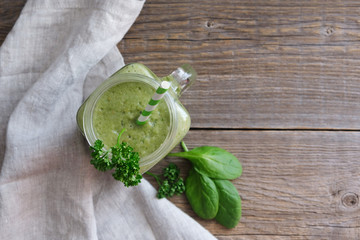 Wall Mural - Top view on a glass of green smoothie and spinach leaves on a wooden background, linen table napkin nearby. Place for text