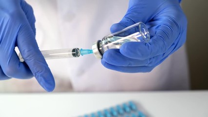 Wall Mural - Doctor or nurse in blue gloves filling the syringe with vaccine for injection close up, vaccination and immunisation concept.