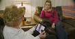 An elderly Caucasian woman and her daughter engaged in a video conference with her doctor via a telehealth or telemed app on a wireless mobile device tablet pc.
