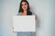 Portrait of young attractive woman holding blank paper against white background, hipster girl holding blank ad poster with copy space for text message about feminism or Save Environment Poster