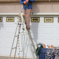 Man stringing Christmas lights on his house.