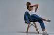 © IC Production - Confident lady in sunglasses in white t-shirt in jeans with denim jacket posing on camera sitting on chair with leg lies on the knee. Fashion concept