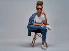 Confident Girl In Sunglasses In White T-shirt In Jeans In Sneakers Posing On Camera Sitting On Chair With Leg Lies On The Leg. Fashion Concept