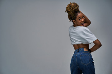 Woman in a white T-shirt in jeans with earrings with braids on her head, turning over her shoulder, stands with her back to the viewer. Denim concept