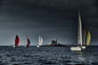 Sailboats compete in a sailing regatta at sunset, sailing race, reflection of sails on water, multi-colored spinaker, boat number aft boats, big white clouds, the island with a lighthouse
