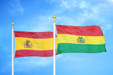 Spain and Bolivia  two flags on flagpoles and blue cloudy sky