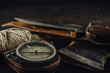 Old military compass, rusty hunting bushcraft knife, small axe and a linen rope on the dark wooden table. Leather cases, front view, survival hunting concept.