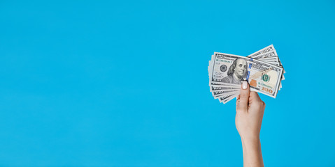 Female hand holding dollar banknotes on blue background. Money and Finance concept. Economic crisis