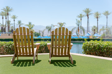 Wooden two chairs by the pool with green artificial grass.