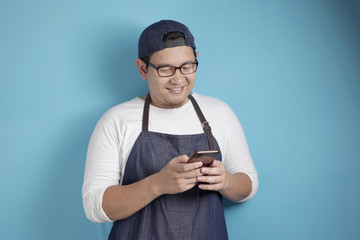 Portrait of happy smiling Asian chef or waiter typing message chat on his phone