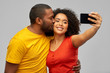 © Syda Productions - technology and people concept - happy smiling african american couple taking selfie by smartphone and kiss over grey background
