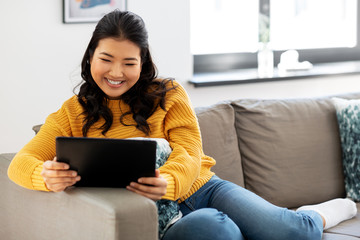 Wall Mural - people and leisure concept - happy smiling asian young woman in yellow sweater with tablet pc computer sitting on sofa at home