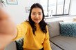 © Syda Productions - people and leisure concept - happy smiling asian young woman in yellow sweater taking selfie at home