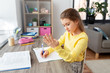 children, education and learning concept - happy student girl with book counting fingers and writing to notebook at home