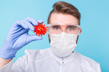 Covid-19, Vaccine development and medicine concept - Man scientist in flu mask and protective gloves holding a model of coronavirus.