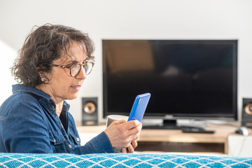 Wall Mural - cheerful brunette senior woman using smartphone while sitting on sofa