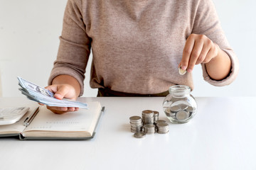 Women are putting coins in a piggy bank, glass bottle, saving money with coins, stepping into a growing business to succeed and save for retirement