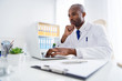 © deagreez - Photo of family doc dark skin guy watch modern technology notebook innovation medical cov viral news look screen online help wear white lab coat sitting chair table office clinic indoors