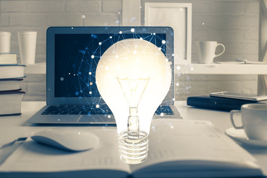 Computer on desktop in office with bulb icon hologram. Multi exposure. Concept of idea.