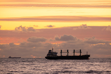 Sunset over the sea. A naval ship on the horizon. Oil tanker ship at sea on a background of sunset sky