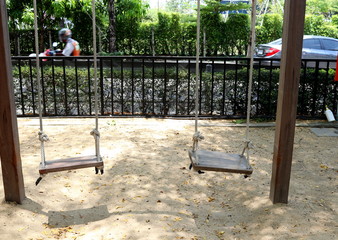 Two wood swing are hanging over ground between wood poles in park, Thailand. Shade and sun light on ground.