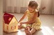 © sementsova321 - Little girl playing with doll house while siiting on floor in bedroom. Role game for young children. Female child putting to bed her toy doll, charming little lady wears yellow dress. Children concept