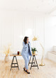 © Елизавета Старкова - A serious business working freelance girl a woman with black hair in a pale blue suit working on a laptop and phone at a wooden Desk against a white wall in the home office