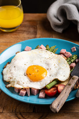 Wall Mural - Healthy breakfast or lunch with fried egg, bread toast, green asparagus and tomatoes on blue plate on old wooden table