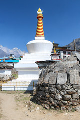 View of typical white stone tibetan buddhist stupa in Himalayas next to mani stones with mantras in Thyanboche village. Clear blue sky. East asian culture theme.