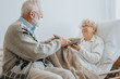 © Photographee.eu - Grey elderly man hands a book to a senior friend lying on a hospital bed