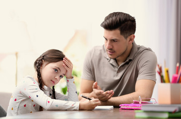 Wall Mural - Father scolding his daughter while helping with homework at table indoors